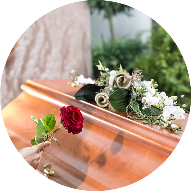 A circular cropped image of a coffin with flowers and a had placing a rose.