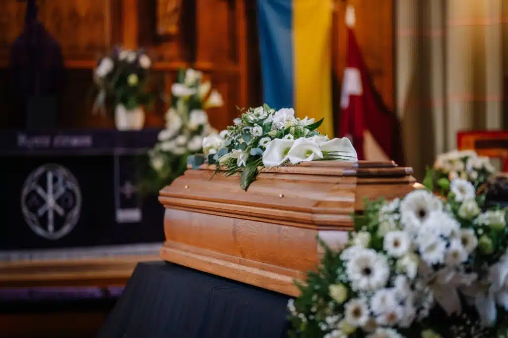 Closed coffin placed within a church during a funeral with flowers around it.